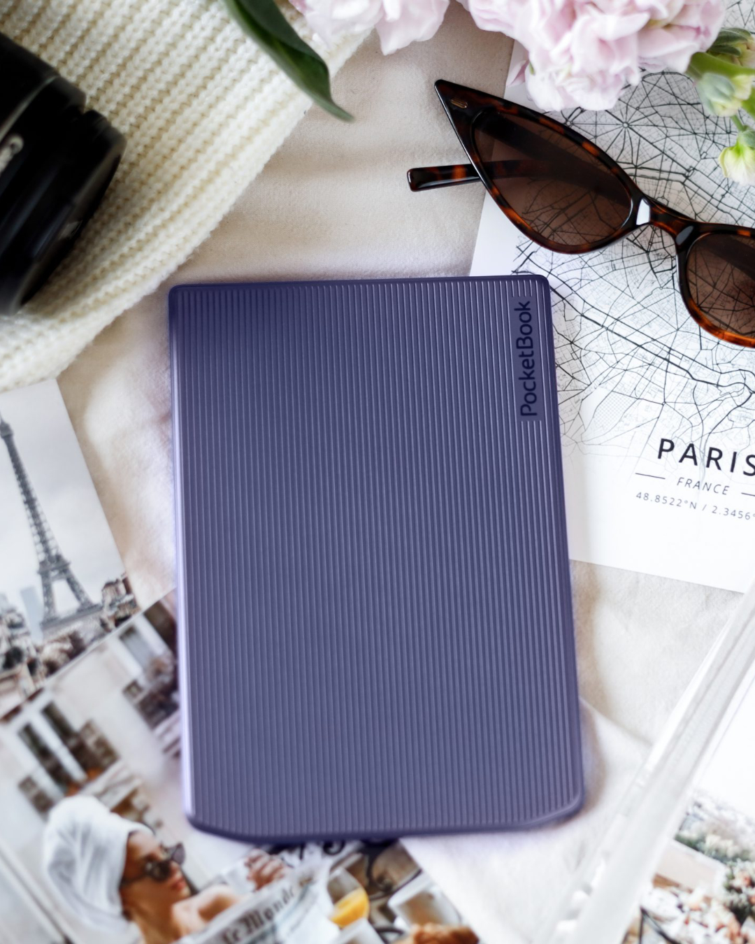 Ein E-Book-Reader liegt auf einem Tisch, umgeben von einer Sonnenbrille und anderen Gegenständen